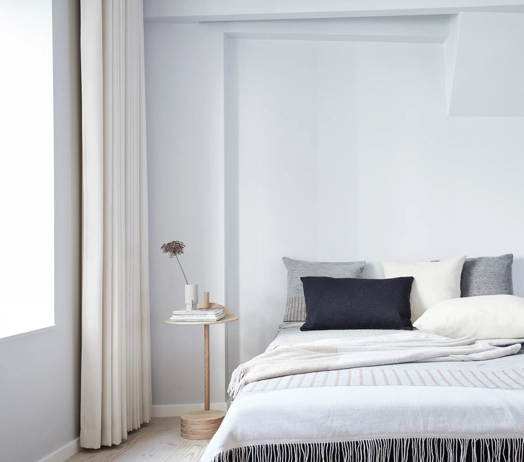 A bedroom with white walls and a FORM & REFINE AYMARA LONG CUSHIONS bed designed by Gestalt Haus.
