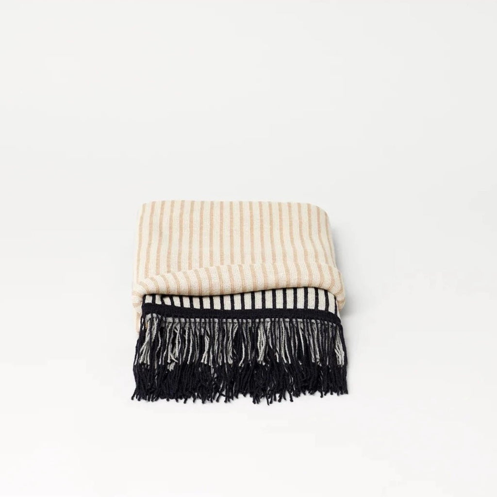 A beige and black striped AYMARA PLAID THROWS blanket with fringes by FORM & REFINE, sold at Gestalt Haus.