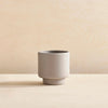 A small grey BOTANY PORCELAIN PLANT POT designed by AARON PROBYN, sitting on top of a wooden table at Gestalt Haus.