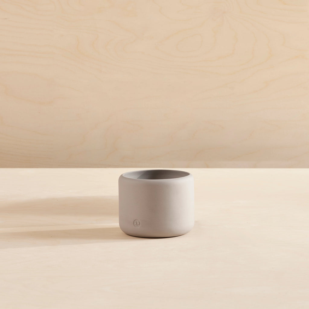 A small Aaron Probyn porcelain plant pot sitting on a table with a beige background, inspired by Gestalt Haus.