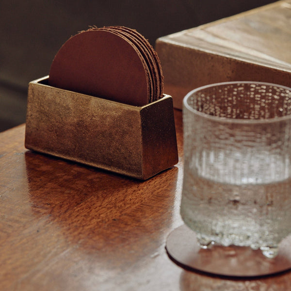 A glass of water on a table next to a COASTER HOLDER WITH COASTERS for Studio Henry Wilson's craftsmanship.
