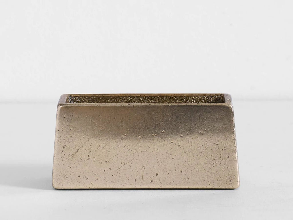 A small BRASS COASTER HOLDER by STUDIO HENRY WILSON on a white surface in Gestalt Haus style.