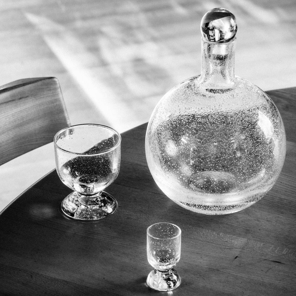 A black and white photo of a Louise Roe Bubble Glass Carafe and a glass on a table at Gestalt Haus.