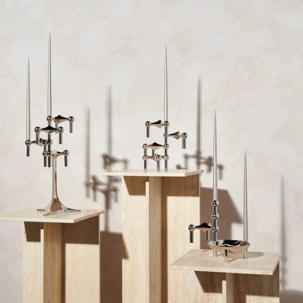 Three STOFF NAGEL candle holders on wooden pedestals in front of a Gestalt Haus wall.