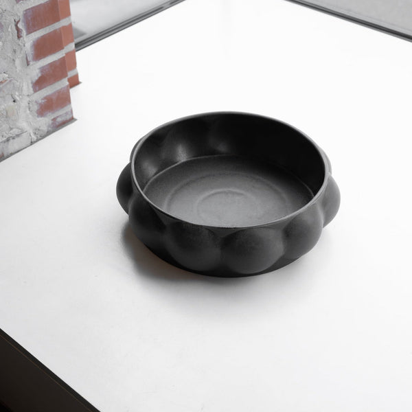 A black CERAMIC BALLOON TRAY sits on a table in front of a window at Gestalt Haus.