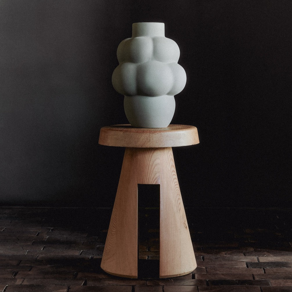 A Louise Roe ceramic balloon vase with a Gestalt Haus inspired design sits on top of a wooden stool.
