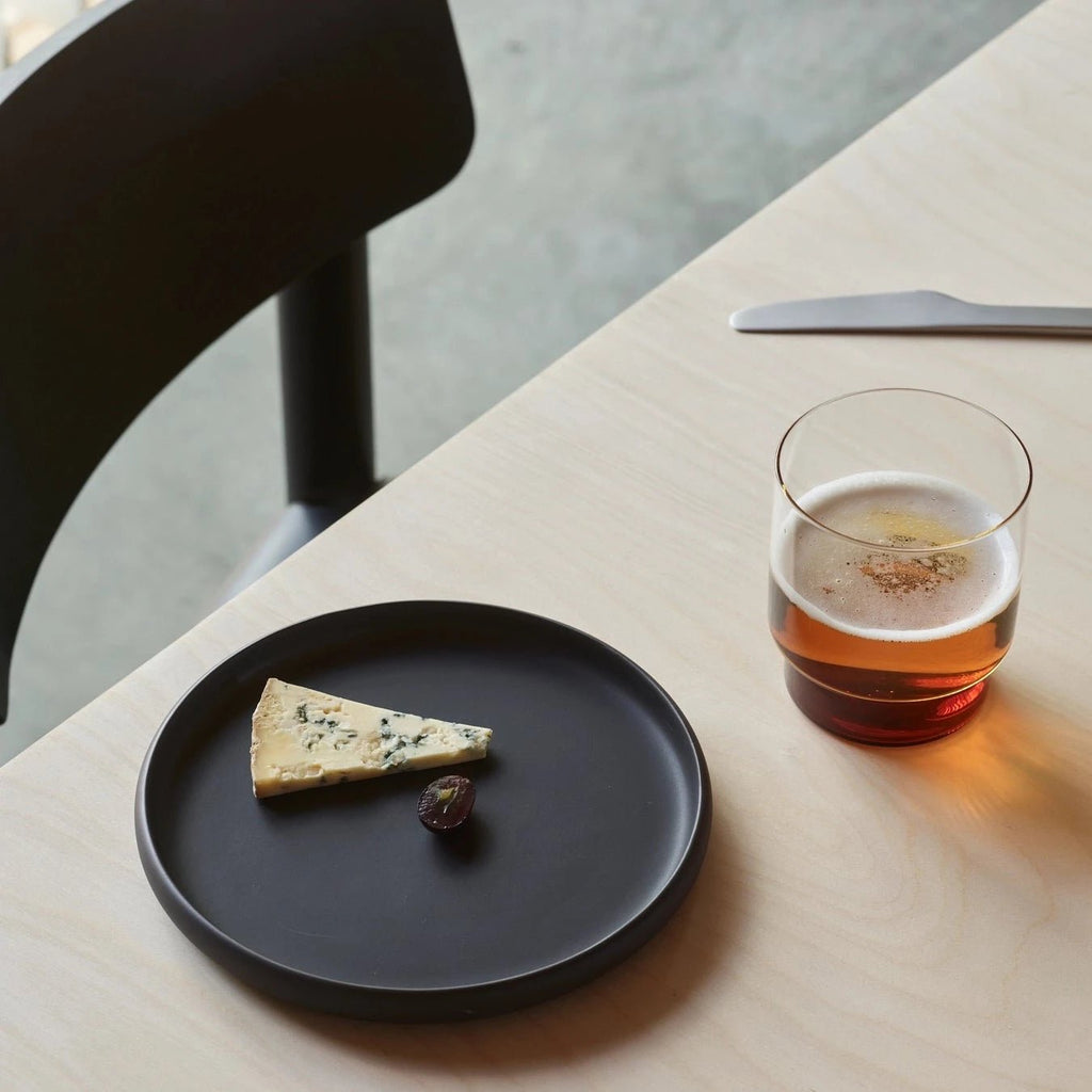 A black COLOMBO TABLEWARE plate with cheese and a glass of beer at Gestalt Haus.