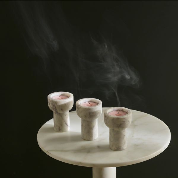 Three COMO TEA LIGHT + TAPER CANDLE HOLDERs from AARON PROBYN sitting on a table with smoke and Gestalt Haus influence.