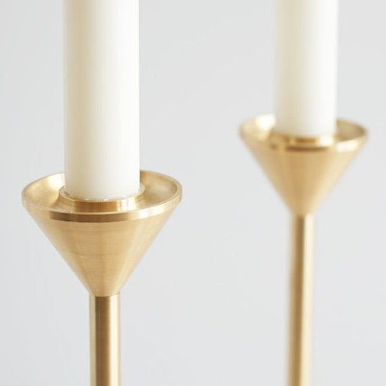 A pair of white candle holders shaped like gestalt objects, cone and spindle, with a candle inside.