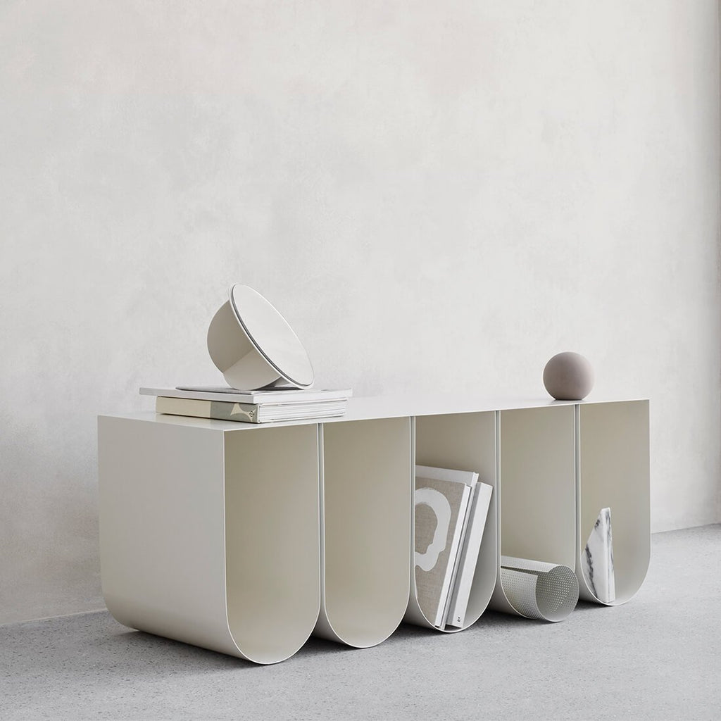 A white curved bench made by Kristina Dam Studio, adorned with books and other items.