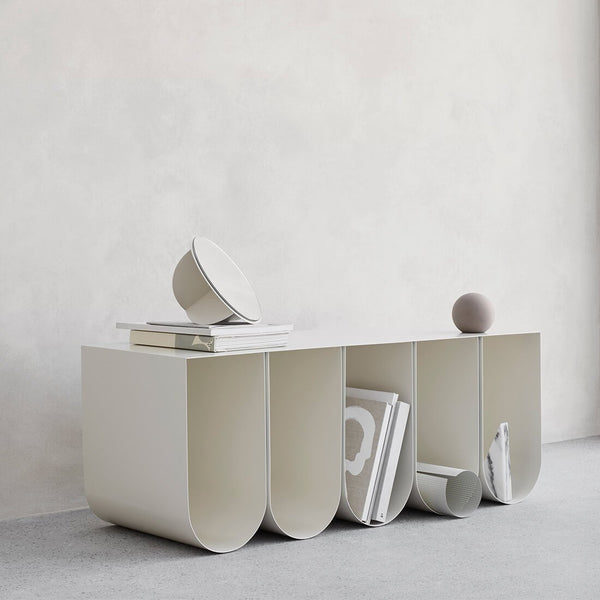 A white curved bench made by Kristina Dam Studio, adorned with books and other items.