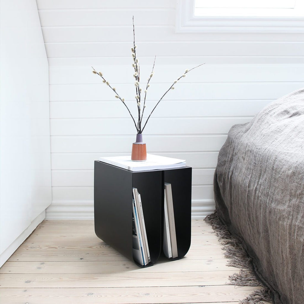 A black CURVED SIDE TABLE from KRISTINA DAM STUDIO adorned with a flower exemplifying Gestalt design principles.