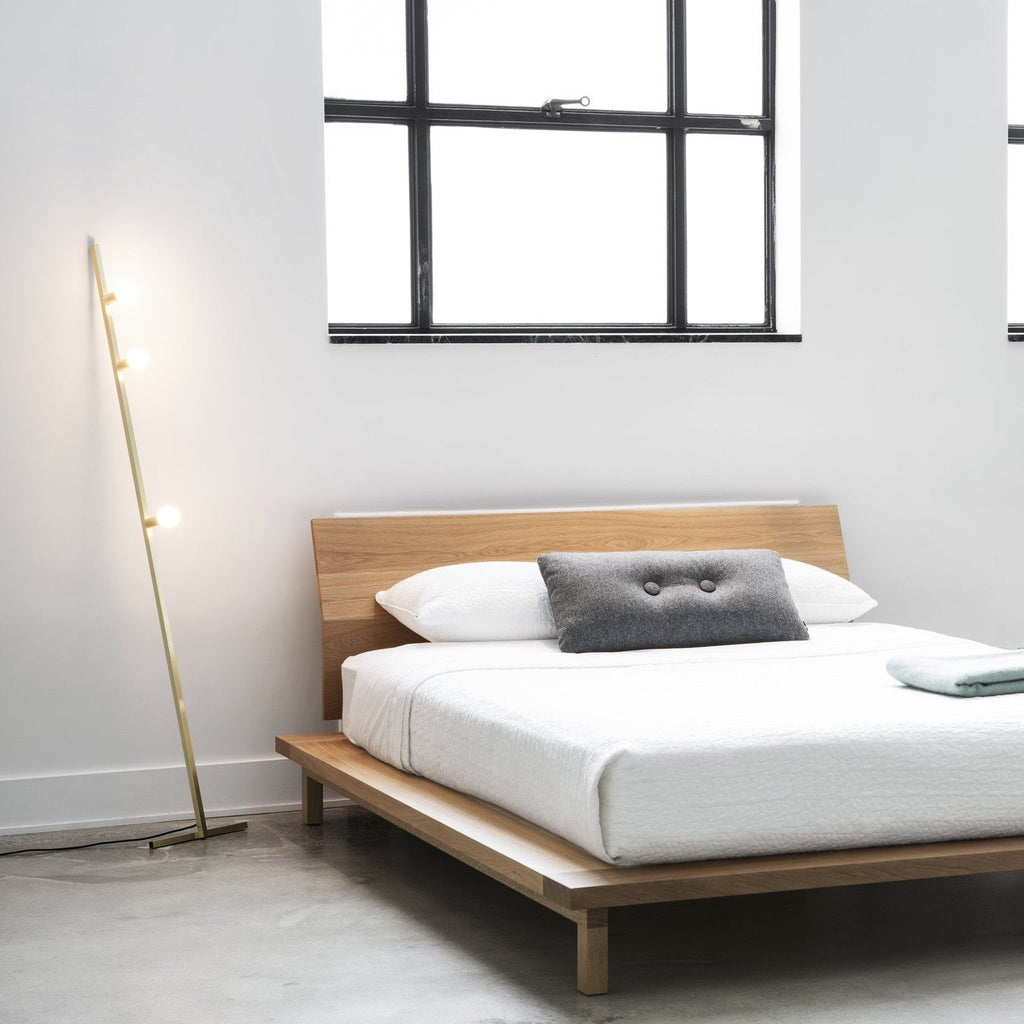 A bed with a wooden frame and a LAMBERT ET FILS DOT LINE FLOOR LAMP on it.