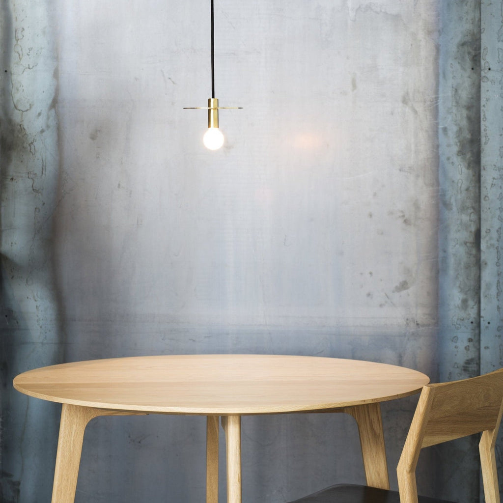 A wooden DOT SUSPENSION table with a light bulb hanging above it from LAMBERT ET FILS in the Gestalt Haus style.