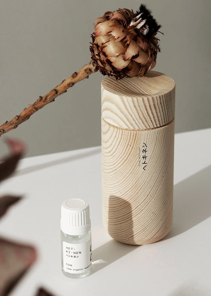 A Hetkinen wooden container with a Gestalt Haus flower and a bottle of Drop Oil Diffusers essential oil.