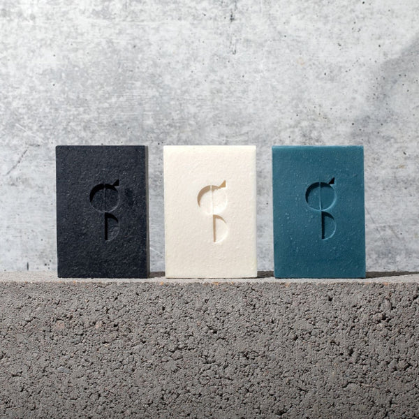 Three Gestalt Haus Bar Soaps displayed on a concrete wall.
