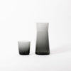 A GLASS CARAFE and a glass cup designed by GARY BODKER DESIGNS on a white surface.