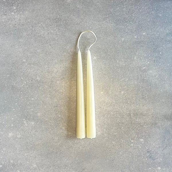 A pair of Danica Designs hand-dipped taper candles on a concrete surface at Gestalt Haus.