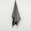 A HAND WOVEN towel from the Gestalt Haus collection hanging on a white wall.