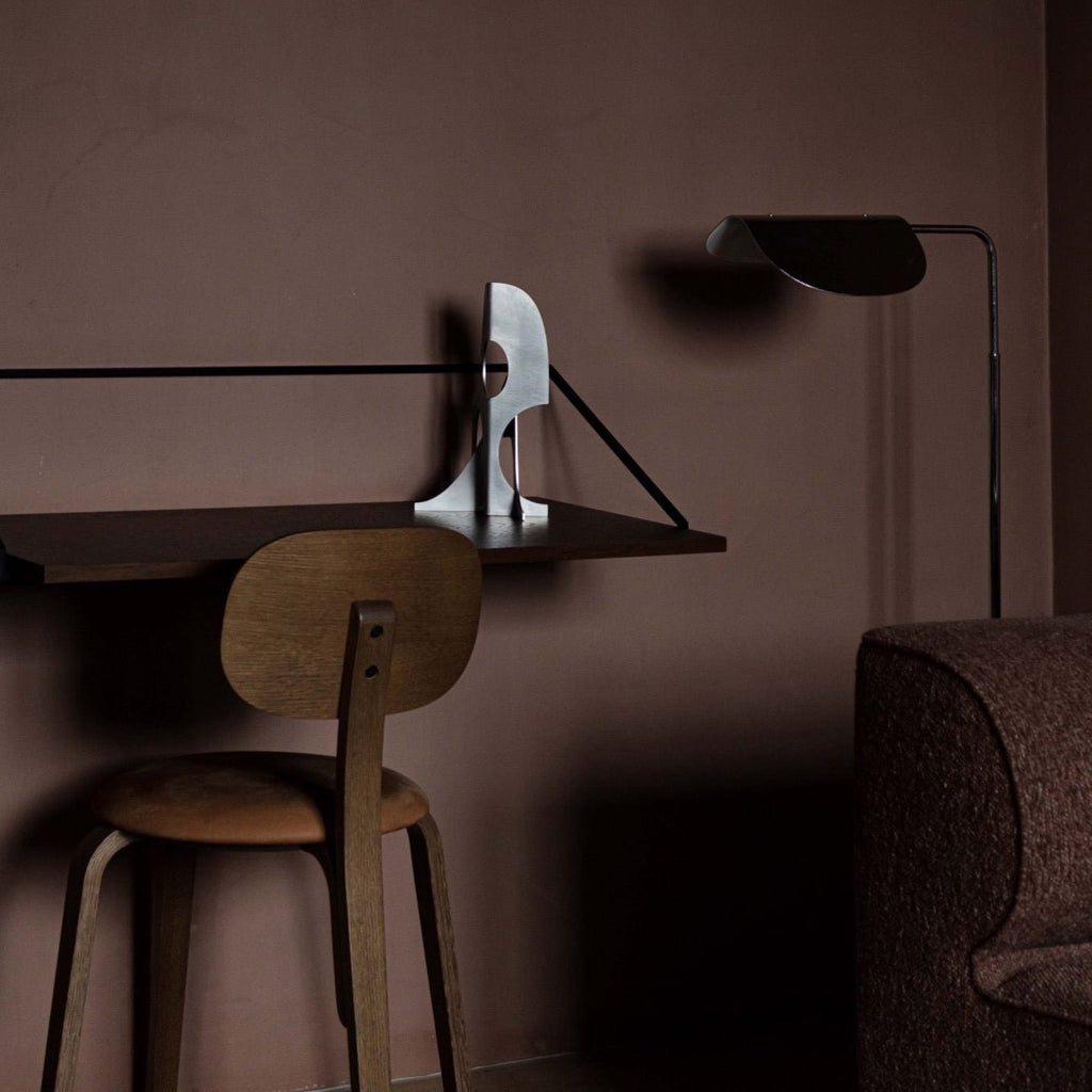 A Gestalt Haus desk with an IN-BETWEEN ELEMENTS 03:45 PM lamp and a chair in a brown room.