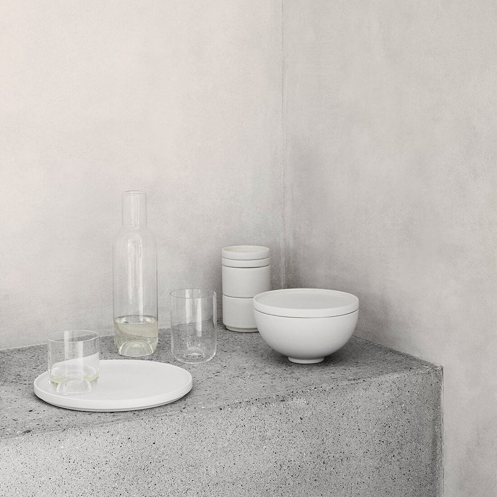 A white capsule carafe, bowl, and glass sit on a concrete wall from Kristina Dam Studio at Gestalt Haus.