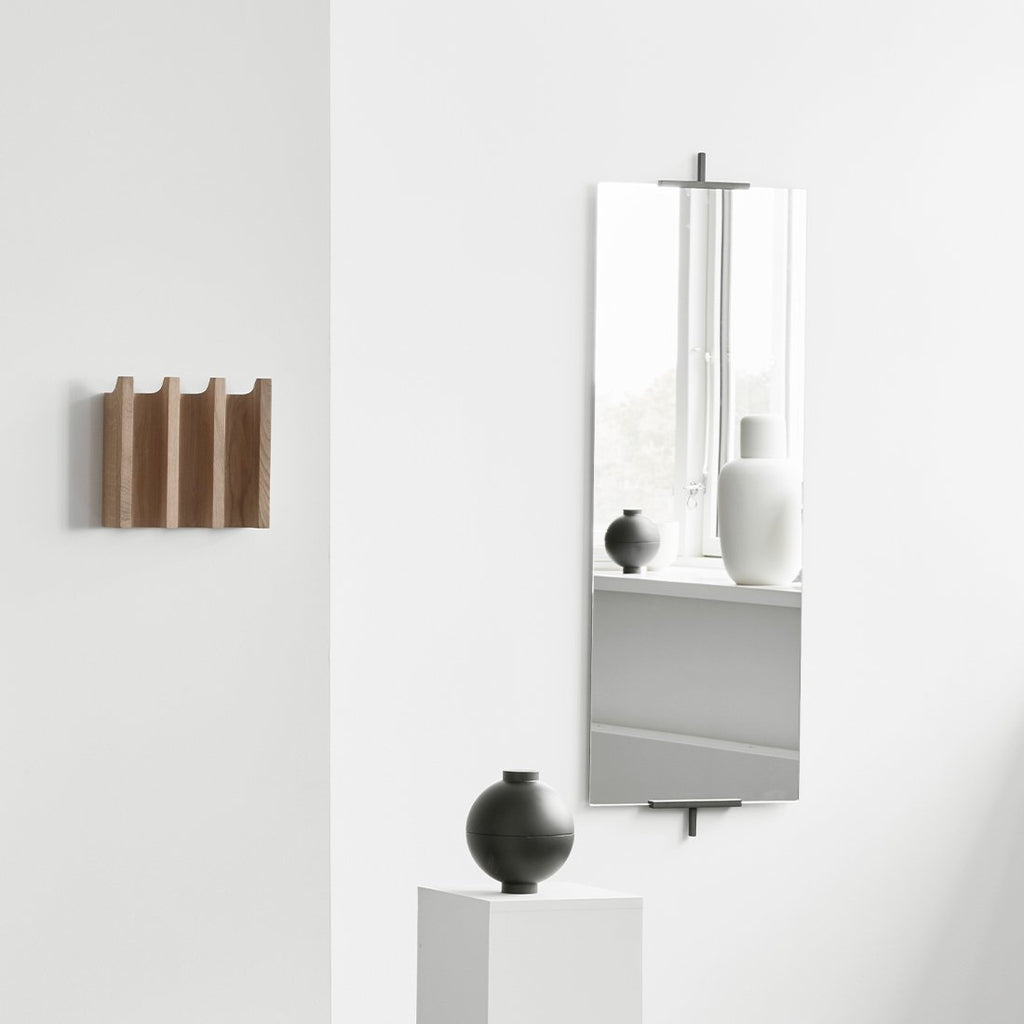 A minimalist Gestalt Haus design featuring a white wall adorned with a distinctive wooden sphere by KRISTINA DAM STUDIO and a sleek mirror.
