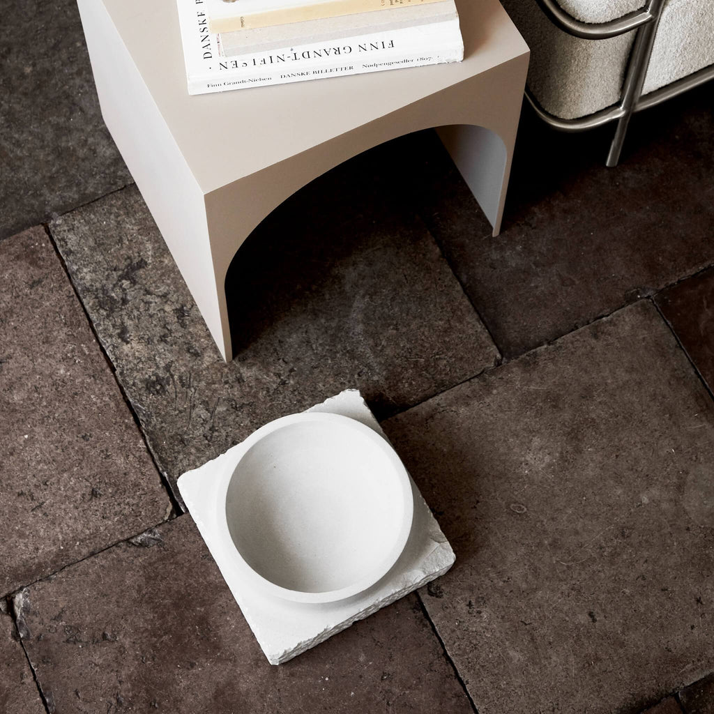 A white bowl from Kristina Dam Studio in the shape of a lacuna sits next to a book on the floor.
