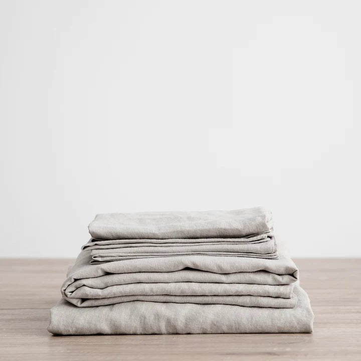 A stack of CULTIVER LINEN sheets on a wooden table in a Gestalt Haus.