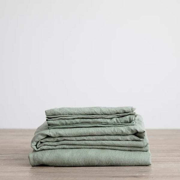 A stack of CULTIVER LINEN SHEET SET (FITTED + FLAT) WITH PILLOWCASES arranged on a wooden table at Gestalt Haus.