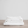 A stack of Gestalt Haus LINEN SHEET SET (FITTED + FLAT) WITH PILLOWCASES on a wooden table.