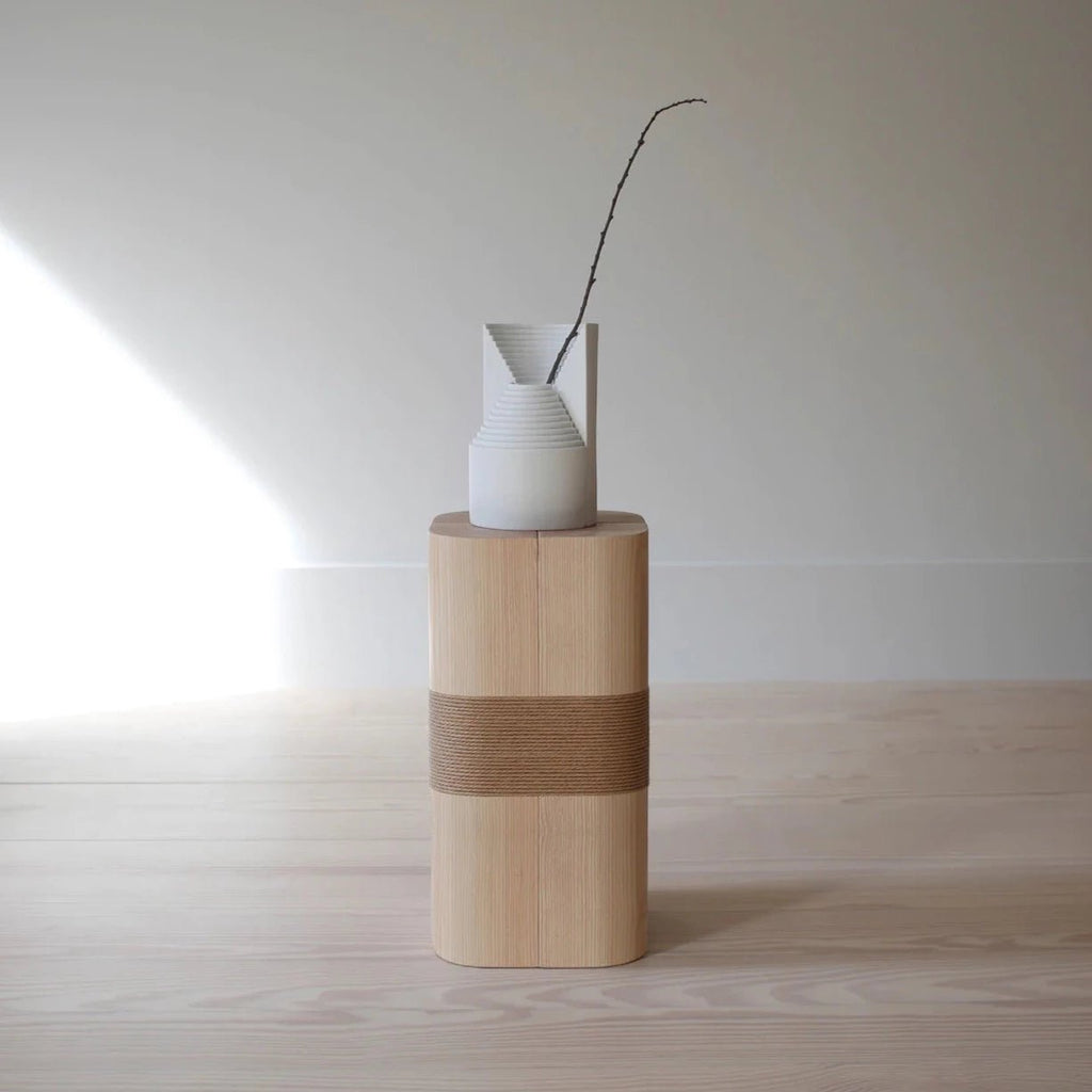A Gestalt Haus MONOLITH PLINTH vase sits on top of an ORIGIN MADE table.