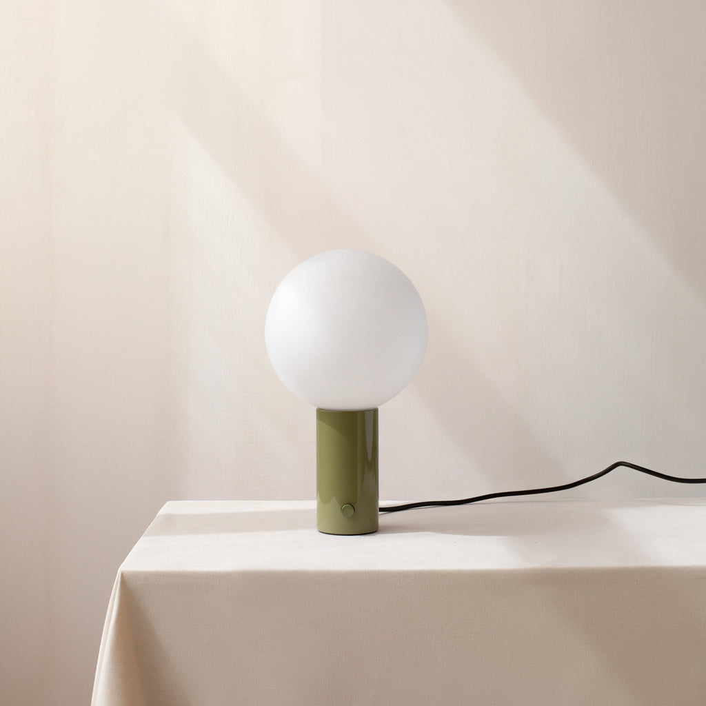An ORB TABLE LAMP from the brand IN COMMON WITH with a green sphere sitting on top of a Gestalt Haus-inspired table.