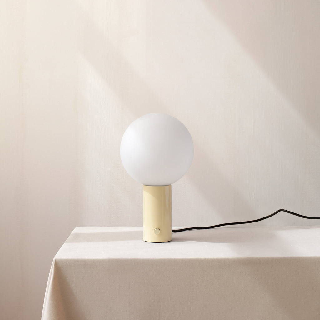 A Gestalt Haus table lamp on a table next to a white tablecloth.