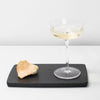 A PASSE-PARTOUT GLASSWARE and a piece of bread on a black tray designed by Vincent Van Duysen for Gestalt Haus.