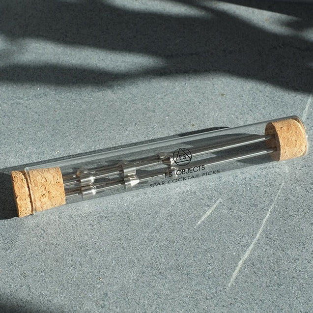 A glass tube with a cork sitting on top of it, called the FS OBJECTS SPAR COCKTAIL PICKS