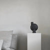 A black SPHERE VASE by 101 COPENHAGEN sits on top of a white pedestal.