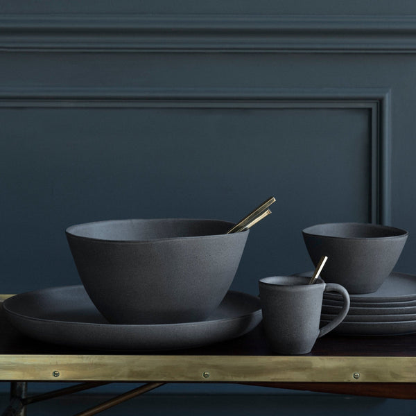 A set of black tableware on a table in front of a blue wall, inspired by Gestalt Haus.
