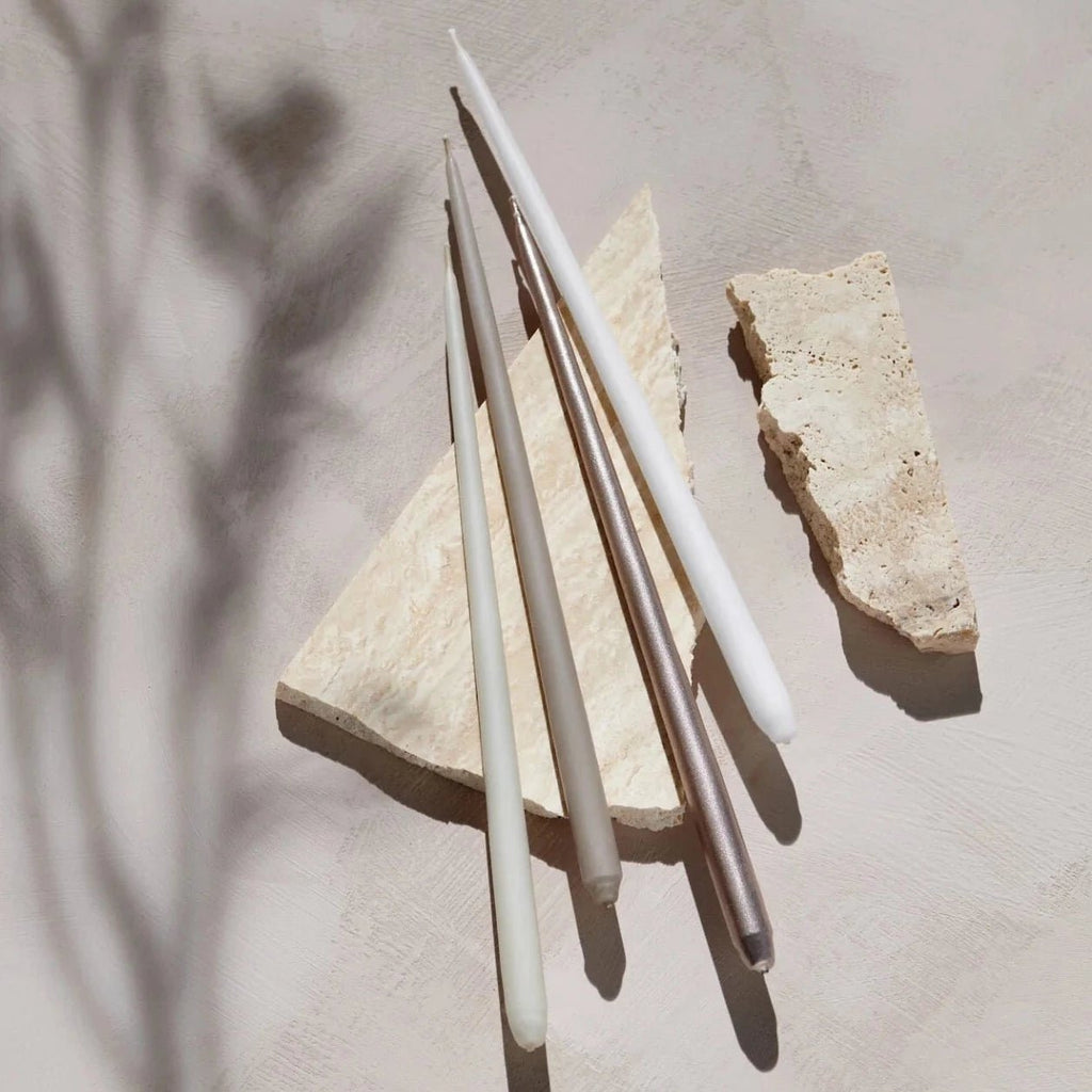 A collection of Gestalt Haus taper candles and a stone on a table.