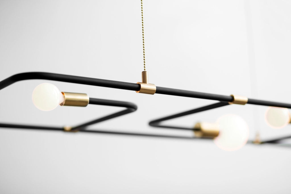 A black and gold THE BEAUBIEN LAMP pendant light hanging on a white wall at Gestalt Haus.
