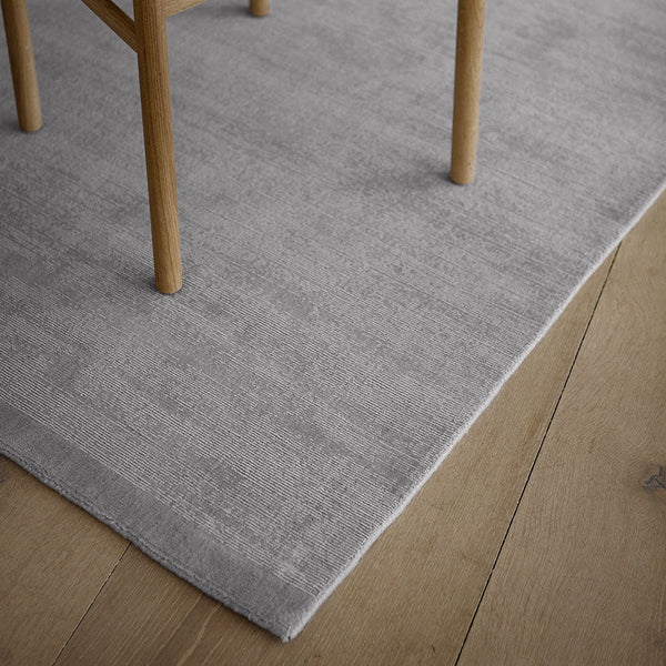 A grey FABULA LIVING rug on a wooden floor with a Gestalt Haus chair.
