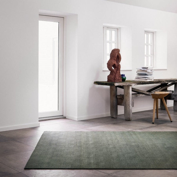 A green THE RUNE RUG from FABULA LIVING placed in a room with white walls showcasing a Gestalt Haus aesthetic.