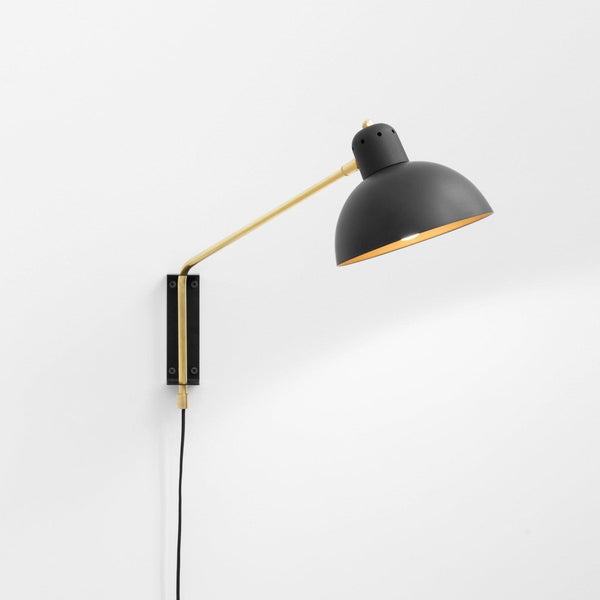 A black and gold Gestalt Haus Waldorf wall lamp on a white wall.