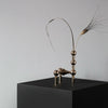 A brass sculpture on a black box, featuring a feather, by STOFF NAGEL.