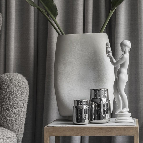 A table displaying a WAVE VASE by KLASSIK STUDIO and a statue in the Gestalt Haus style.