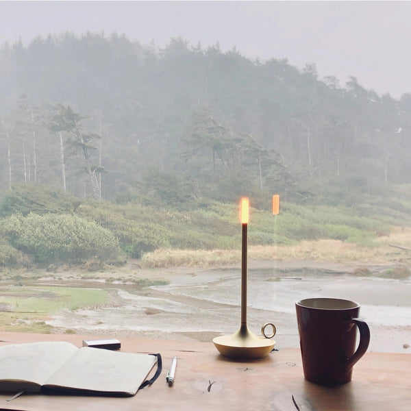 A cup of coffee and a Graypants notebook on a table next to a lake at Gestalt Haus.